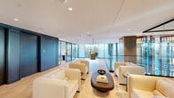 Located at 3030 Potomac Ave in Arlington, VA, this thoughtfully designed single-floor office amenity space offers a compelling blend of functionality and contemporary style. The layout encompasses a generous footprint that accommodates multiple distinct zones, each serving a specific purpose while contributing to a cohesive, upscale aesthetic.

The central lounge area features plush cream-upholstered armchairs arranged around a sculptural dark wood coffee table, set atop a textured area rug. Floor-to-ceiling glass walls and expansive windows flood the space with natural light and offer sweeping views of the surrounding Arlington streetscape and greenery.

A standout design feature throughout is the suspended swing chairs — dramatic leather hanging seats mounted from the ceiling — adding a bold, playful element to the otherwise refined interior. The herringbone-patterned hardwood floors tie the space together, running seamlessly through each zone.

Private workstations, framed by floor-to-ceiling windows, provide focused work areas outfitted with built-in desks and print services. Glass-partitioned conference rooms with black steel frames offer transparency while maintaining acoustic separation, accommodating collaborative meetings with ease.

Throughout, recessed lighting, warm wood accents, open shelving, and carefully curated furnishings create a professional yet inviting atmosphere suited for productivity and connection.
