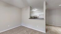 This single-floor, one-bedroom unit offers a practical and comfortable layout across a compact yet efficiently designed floor plan. The entry foyer greets residents with durable wood-style flooring and a large window fitted with blinds that allows natural light to filter in while providing a view of the surrounding greenery outside.

The galley-style kitchen is thoughtfully arranged with ample white cabinetry lining both walls, dark countertops, a built-in range, a refrigerator, and a sink — all finished with wood-style flooring that adds warmth to the space. A pass-through counter opens the kitchen directly to the living room, creating a connected, open feel that is ideal for everyday living.

The carpeted living room is bright and open, benefiting from the kitchen pass-through and providing a versatile space for a variety of furniture arrangements.

The primary bedroom is a well-sized, carpeted retreat with a window offering natural light and outdoor views. It connects to a walk-in closet featuring built-in shelving along the walls, providing generous storage space.

Throughout the unit, neutral gray walls, white trim, and consistent flooring choices create a clean, cohesive aesthetic. The overall ambiance is light, functional, and move-in ready.