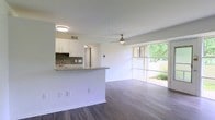 This single-floor residence at 1055 112 offers a clean, modern living experience defined by an open-concept layout that seamlessly connects the kitchen and living areas. The kitchen features crisp white cabinetry, a dark tile backsplash, granite countertops, and a breakfast peninsula that doubles as a casual dining and prep space. A stainless steel sink adds a refined, contemporary touch. The living area is anchored by rich, dark hardwood-style flooring that runs throughout, creating a warm contrast against the bright white walls and ceilings. A modern ceiling fan with a brushed nickel finish adds both style and comfort to the main living space. Floor-to-ceiling windows and a sliding glass door flood the interior with natural light while offering direct views of lush greenery outside, blending indoor and outdoor living effortlessly. The overall ambiance is light, airy, and move-in ready, with a neutral palette that provides a versatile backdrop for any décor style. Clean lines, updated fixtures, and thoughtful finishes throughout make this a well-appointed and inviting space.