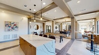 Located at 1880 Maple Dr NW in Kennesaw, Georgia, this single-floor community amenity space is a thoughtfully designed gathering hub that blends modern aesthetics with versatile social functionality. The open-plan layout is anchored by a dramatic marble-topped island bar, adorned with bold veining and surrounded by stylish upholstered barstools, all beneath sleek pendant lighting that draws the eye upward to the coffered ceiling detail above.

The space flows seamlessly across large-format tile flooring with contrasting inlay patterns, connecting distinct activity zones. A formal dining area features a long communal table with contemporary seating and an elegant chandelier, bathed in natural light from floor-to-ceiling windows overlooking the exterior. Adjacent lounge areas offer plush curved chairs arranged around low coffee tables, creating intimate conversation spaces.

Entertainment is central to the design, with a full-size billiards table and a regulation shuffleboard court providing lively recreation options. A dedicated media wall with a large-screen display and a wet bar area with cabinetry rounds out the amenities. Curated artwork, round mirrors, and warm accent lighting contribute to a refined yet welcoming ambiance throughout, making this a dynamic and well-appointed communal destination.