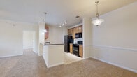 This two-floor residence offers a thoughtfully designed layout with a warm, neutral color palette throughout. The open-concept living and dining area is generously proportioned, featuring plush carpeting, crown molding, a ceiling fan with light fixture, and a window that invites natural light and outdoor views. The kitchen is efficiently arranged and open to the living space via a peninsula with dark granite countertops. Warm honey-toned cabinetry provides ample storage, while black appliances — including a refrigerator, electric range, built-in microwave, and dishwasher — complement the dark countertops. Track lighting illuminates the kitchen, and pendant lights add a finishing touch above the peninsula. The bathroom is well-appointed with a full soaking tub and shower combo, white tile surround accented by a decorative taupe tile border, rich wood cabinetry, dark granite vanity countertop, and tile flooring. Bedrooms are carpeted and offer a clean, open feel, with one featuring a spacious walk-in closet outfitted with wire shelving. A dedicated laundry room with full-size washer and dryer hookups and additional shelving adds practical convenience to the home.