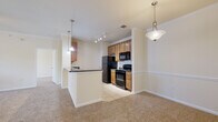 This two-floor residence offers a thoughtfully designed layout with a warm, neutral color palette throughout. The open-concept living and dining area is generously proportioned, featuring plush carpeting, crown molding, a ceiling fan with light fixture, and a window that invites natural light and outdoor views. The kitchen is efficiently arranged and open to the living space via a peninsula with dark granite countertops. Warm honey-toned cabinetry provides ample storage, while black appliances — including a refrigerator, electric range, built-in microwave, and dishwasher — complement the dark countertops. Track lighting illuminates the kitchen, and pendant lights add a finishing touch above the peninsula. The bathroom is well-appointed with a full soaking tub and shower combo, white tile surround accented by a decorative taupe tile border, rich wood cabinetry, dark granite vanity countertop, and tile flooring. Bedrooms are carpeted and offer a clean, open feel, with one featuring a spacious walk-in closet outfitted with wire shelving. A dedicated laundry room with full-size washer and dryer hookups and additional shelving adds practical convenience to the home.