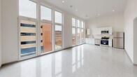 Located at 80 Middlesex St in Lowell, MA, this one-bedroom, one-bathroom unit offers a thoughtfully designed single-floor layout with a clean, contemporary aesthetic throughout. The living and kitchen area is the undeniable highlight of the space, featuring dramatic floor-to-ceiling windows that flood the interior with natural light and frame sweeping views of Lowell's historic urban streetscape. Soaring ceilings amplify the sense of openness, while polished terrazzo flooring runs seamlessly throughout, adding a refined, modern touch. The kitchen is outfitted with white cabinetry, stainless steel appliances including a range, microwave, and dishwasher, and a functional sink workspace. Recessed lighting complements the abundant natural light across the main living area. The bedroom is a well-proportioned retreat featuring a built-in double closet, a large window with outdoor views, and the same terrazzo flooring carried throughout the unit. The hallways connect the spaces with a clean, uncluttered flow. The bathroom is finished in an all-white palette, featuring a full soaking tub with an overhead shower, built-in shelving, and brushed nickel fixtures. The overall ambiance is bright, minimalist, and modern, offering a polished urban living experience in the heart of Lowell.