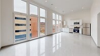 Located at 80 Middlesex St in Lowell, MA, this one-bedroom, one-bathroom unit offers a thoughtfully designed single-floor layout with a clean, contemporary aesthetic throughout. The living and kitchen area is the undeniable highlight of the space, featuring dramatic floor-to-ceiling windows that flood the interior with natural light and frame sweeping views of Lowell's historic urban streetscape. Soaring ceilings amplify the sense of openness, while polished terrazzo flooring runs seamlessly throughout, adding a refined, modern touch. The kitchen is outfitted with white cabinetry, stainless steel appliances including a range, microwave, and dishwasher, and a functional sink workspace. Recessed lighting complements the abundant natural light across the main living area. The bedroom is a well-proportioned retreat featuring a built-in double closet, a large window with outdoor views, and the same terrazzo flooring carried throughout the unit. The hallways connect the spaces with a clean, uncluttered flow. The bathroom is finished in an all-white palette, featuring a full soaking tub with an overhead shower, built-in shelving, and brushed nickel fixtures. The overall ambiance is bright, minimalist, and modern, offering a polished urban living experience in the heart of Lowell.