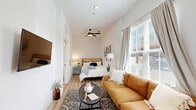 Located at 421 W Tremont Ave in Charlotte's vibrant Dilworth neighborhood, this thoughtfully designed one-bedroom, one-bathroom unit makes excellent use of its compact footprint. The open-concept layout connects the kitchen and living area seamlessly, creating a functional and inviting space bathed in natural light from multiple windows with blinds and sheer curtains.

The kitchen is a standout feature, boasting slate-blue shaker-style cabinetry accented with brushed gold hardware, white subway tile backsplash, stainless steel appliances including an electric range with over-the-range microwave, and a stainless steel sink with a matte black faucet. Light wood-look flooring flows throughout the entire unit, adding warmth and visual continuity.

The living and sleeping areas share an open, elongated space complete with a ceiling fan and wall-mounted TV. Large windows invite generous natural light, while crisp white walls contribute to a bright, airy ambiance. The bedroom area is well-proportioned, offering comfortable accommodations.

The bathroom features a clean, all-white design with a single vanity with white cabinetry, a large mirror, and a tub-shower combination with white subway tile surround and a curved curtain rod. Every detail reflects a modern yet welcoming aesthetic, making this unit a well-appointed residence in a prime Charlotte location.