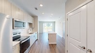Located at 409 Pelham Rd in Greenville, SC, this well-appointed one-bedroom, one-bathroom residence offers a thoughtfully designed single-floor layout with a clean, contemporary aesthetic throughout. The open-concept kitchen and living area serves as the heart of the home, where warm hardwood-style flooring extends seamlessly from the kitchen to the living space. The kitchen is outfitted with light wood-grain cabinetry, white quartz countertops, a classic subway tile backsplash, and a full suite of stainless steel Whirlpool appliances, including a refrigerator, range, microwave, and dishwasher. A center island provides additional prep and dining space. The living area is bright and airy, with a sliding glass door that opens to a private balcony with outdoor views, allowing natural light to fill the room. The bedroom features plush carpeting, a ceiling fan, and large windows that bring in generous natural light while overlooking the surrounding greenery. A dedicated walk-in closet with wire shelving offers ample storage. The bathroom includes a full soaking tub with an overhead shower and clean white surroundings. Recessed lighting throughout the unit adds a polished, modern finish to this inviting Greenville residence.