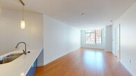 Located at 120 Kingston St in the heart of Boston, MA, this modern single-floor residence offers a thoughtfully designed open layout with clean lines and a bright, contemporary aesthetic throughout. Warm hardwood flooring flows seamlessly across the living and sleeping areas, complementing the crisp white walls and creating a welcoming, cohesive atmosphere.

The spacious living area is bathed in natural light through large floor-to-ceiling windows that frame striking views of the surrounding downtown Boston skyline, bringing the energy of the city indoors. The open-concept design connects the living space directly to the kitchen, which features sleek white cabinetry extending to the ceiling, stainless steel appliances including a refrigerator, range, and microwave, a white quartz countertop, and a navy blue island that serves as a functional focal point and visual accent.

A well-proportioned bedroom also benefits from generous window exposure, offering additional city views and ample natural light. The bathroom is finished in a modern style with large-format tile flooring, a floating dark wood vanity, a backlit mirror, and a clean, open shower area. Additional storage is provided by a dedicated closet off the kitchen area. The overall design emphasizes simplicity, functionality, and urban sophistication throughout.