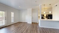 This single-story, 3-bedroom, 2-bathroom home offers a thoughtfully designed layout that maximizes comfort and functionality. The open-concept living and kitchen area serves as the heart of the home, featuring durable wood-look flooring, crown molding, and recessed lighting throughout. The kitchen is equipped with black appliances, white cabinetry, a striking quartz-topped peninsula with pendant lighting, and a tile backsplash — all flowing seamlessly into the living space. A sliding glass door and flanking windows in the living area invite abundant natural light and provide access to the outdoors. The primary bedroom offers a ceiling fan and a spacious walk-in closet with built-in shelving and hanging rods. Each bedroom maintains the consistent wood-look flooring found throughout the home. The bathrooms are finished with white cabinetry, quartz countertops, and a tiled tub-shower combination accented with a decorative mosaic border. Additional conveniences include a dedicated laundry room, a pantry, and three closets for ample storage. A connected hallway efficiently links all rooms, creating a cohesive and practical single-floor living experience.