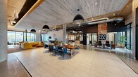 Located at 2219 E 11th St in Tulsa, Oklahoma, NOMA is a thoughtfully designed commercial space that masterfully merges industrial and contemporary aesthetics across a single, generously proportioned floor. The open-plan layout is anchored by exposed concrete columns, polished concrete floors, and wood-paneled ceilings that lend warmth and texture throughout. Expansive floor-to-ceiling windows and glass-paneled entry doors flood the interior with natural light while framing views of the surrounding streetscape.

The main communal area features a striking mix of materials — large-format tile, polished concrete, and hardwood — and is furnished with bold, curated pieces including mustard-yellow sofas, a live-edge communal table with blue velvet chairs, and layered area rugs that define distinct gathering zones. A cozy lounge area centers around a suspended fireplace and is complemented by a branded NOMA feature wall with decorative signage.

A dedicated private workspace, enclosed by full-height glass partitions with black steel frames, provides a focused work environment alongside the collaborative open areas. An artistic textured accent wall and warm pendant lighting enhance a secondary seating alcove near the elevator lobby. A dedicated event or flex room with polished concrete floors and NOMA-branded glass doors adds further versatility to this dynamic, well-appointed space.