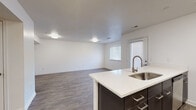 This single-floor residence offers a clean, modern aesthetic with a thoughtfully designed open-concept layout. The kitchen serves as a central hub, featuring dark espresso-toned cabinetry with brushed nickel hardware, crisp white countertops, stainless steel appliances including a dishwasher and range, and a kitchen island with an integrated sink. The kitchen flows seamlessly into a spacious living area finished with wood-look hard flooring, white walls, and recessed lighting, creating a bright and cohesive common space. Natural light enters through multiple windows dressed with horizontal blinds, and a door provides convenient exterior access.

The bedrooms are carpeted for comfort and feature ample natural light from multiple windows. At least one bedroom includes a walk-in closet, while another offers a standard reach-in closet — both providing practical storage solutions. Two full bathrooms serve the residence; one features a dark vanity with white countertop, a large mirror, and a shower-tub combo, while the second is a more compact full bath also equipped with a tub and shower. Wood-look flooring carries through both bathrooms, maintaining a consistent design language. Overall, the space presents a contemporary, move-in-ready environment with a neutral palette and functional layout.