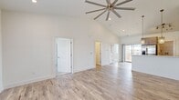 This single-story home in Opelika, Alabama offers five bedrooms, two bathrooms, and a utility room across a efficiently designed floor plan. The open living area immediately impresses with soaring vaulted ceilings, recessed lighting, and a large statement ceiling fan, all complemented by light-toned hardwood-style flooring that extends throughout the main living spaces. Natural light flows in generously through large windows, enhancing the home's clean, bright aesthetic with crisp white walls throughout.

The kitchen features a peninsula with pendant lighting, taupe cabinetry, stainless steel appliances including a French door refrigerator and microwave, and a marble-look tile floor that transitions seamlessly into the living area. A sliding glass door provides direct outdoor access from the kitchen.

The bedrooms are well-proportioned, with the primary bedroom offering notable space, ceiling fans, and windows with views to the exterior. Several bedrooms feature soft carpet flooring, while others showcase the same hardwood-style planks found in the main living areas.

Both bathrooms are finished with striking marble-look porcelain tile on the floors and surrounding the tub-shower combinations, paired with dark-topped vanities featuring vessel sinks and modern hardware, creating an elevated, contemporary feel throughout.