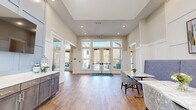 Located at 1421 Rural Hill Rd in Nashville, TN, the Novo Airport Highlands clubhouse is a thoughtfully designed single-floor community facility offering a generous and welcoming atmosphere. The space is anchored by a bright, open entry foyer framed by floor-to-ceiling glass double doors and transom windows that flood the interior with natural light. Warm hardwood-style flooring runs throughout, complementing the neutral, contemporary color palette of soft whites and beiges.

The main lounge area impresses with soaring double-height ceilings accented by exposed wood beams, creating a dramatic yet inviting ambiance. An expansive wall of oversized windows lines this space, offering sweeping outdoor views and maintaining a light-filled environment throughout the day. Flexible seating arrangements — including plush sofas, accent chairs, high-top tables, and booth-style seating — accommodate both social gatherings and casual relaxation.

A dedicated entertainment zone features a pool table and a large wall-mounted television surrounded by stylish lounge seating, ideal for recreation and community events. A built-in refreshment counter with cabinetry adds convenience near the entry area. Classic wainscoting and recessed lighting lend architectural refinement throughout, making this clubhouse a polished and functional hub for the Novo Airport Highlands community.