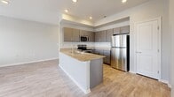 This thoughtfully designed 1-bedroom, 1-bathroom unit offers an efficient and comfortable single-floor layout. Light-toned luxury vinyl plank flooring flows consistently throughout every room, creating a cohesive and clean aesthetic. The open-concept kitchen and living area serves as the heart of the unit, with the kitchen showcasing granite countertops, a peninsula with an integrated sink, taupe flat-front cabinetry, and a full suite of stainless steel appliances including a refrigerator, electric range, microwave, and dishwasher. Recessed lighting illuminates the space, while a sliding glass door with vertical blinds and an adjacent window bathe the living area in natural light. The bedroom is a comfortable, well-proportioned retreat featuring a ceiling fan, two windows with blinds that allow for ample natural light, and a dedicated closet. The full bathroom is finished with a quartz-topped vanity with grey cabinetry, a tub-shower combination with a window above, and light-filled surroundings. A hallway connects the main living areas to the private quarters, with neutral grey walls and clean white trim lending the entire unit a bright, modern, and move-in-ready appearance.