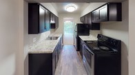 Located at 11580 Somerset Dr in North Royalton, Ohio, this single-floor residence offers a well-organized layout with a variety of thoughtfully appointed spaces. The living area is generously sized, featuring plush carpeting, neutral-toned walls with a two-tone paint scheme, and a large sliding glass door framed by vertical blinds that floods the room with natural light and provides a pleasant view of lush greenery outside. A chandelier adds a decorative touch to the dining area adjacent to the living space. The galley-style kitchen is well-equipped, showcasing dark cabinetry, light granite-style countertops, hardwood-style flooring, and black appliances including a range and refrigerator, with a window at the far end offering additional natural light. The bedrooms are carpeted and bright, each featuring windows with outdoor views and ample closet space. The primary bedroom includes direct access to an en-suite bathroom with a glass-enclosed shower, dark vanity cabinetry, and granite-style countertops. A second full bathroom features a soaking tub with mosaic tile surround, a sleek white vanity, and wood-look flooring. A dedicated laundry area houses a full-size washer and dryer alongside a water heater, providing added convenience within the unit.