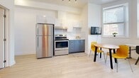 Located at 2238 Rue du Souvenir in Montréal, this efficiently designed 2-bedroom, 1-bathroom unit makes excellent use of its compact footprint. The open-plan kitchen and dining area serves as the heart of the space, featuring two-tone cabinetry with crisp white upper cabinets and slate-blue lower cabinets, a white tile backsplash, and stainless steel appliances including a full-size refrigerator and electric range. Light wood-style flooring runs throughout, enhancing the bright, airy atmosphere. Natural light filters in through several windows, with a bay-style window in the dining area offering pleasant neighbourhood views. A wall-mounted TV and a round dining table with vibrant yellow chairs add functional and modern touches to the living area. The two bedrooms are thoughtfully appointed with clean white walls and the same light flooring, providing a calm and restful environment. The primary bedroom offers a comfortable layout, while the second bedroom is cozy and well-suited as a single room. The bathroom is finished in an all-white palette, featuring large-format horizontal tiles in the shower-tub surround, a single vanity with mirror, and dark floor tiles that provide a subtle contrast. Overall, the unit presents a clean, modern, and functional aesthetic.