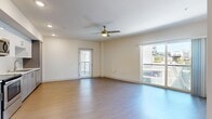 Located in the vibrant Arts District of Los Angeles, this one-bedroom, one-bathroom unit at 950 E 3rd St offers a well-designed, efficiently laid-out single-floor residence. The open-concept kitchen and living room serves as the heart of the unit, featuring light hardwood-style flooring, recessed lighting, and a ceiling fan with light fixture. The kitchen is equipped with stainless steel appliances, including a refrigerator, range, and microwave, complemented by grey cabinetry, white upper cabinets, and a decorative tile backsplash. Multiple sliding glass doors and large windows throughout the living area flood the space with natural light and provide views of the surrounding Los Angeles cityscape. The bedroom is carpeted for comfort, includes its own ceiling fan and window with blinds, and connects to a dedicated walk-in closet outfitted with wire shelving and hanging rods. The bathroom features a full tub-shower combination with white subway tile surround, tile flooring, and white cabinetry for storage. Additional conveniences include an in-unit laundry area and a hallway connecting the main living spaces. The unit's clean, modern finishes and bright, neutral palette create a functional and comfortable urban living environment.