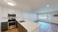 Located at 14960 Sherman Way in Van Nuys, California, this single-floor unit offers a clean, modern aesthetic with thoughtful updates throughout. The open-concept living and kitchen area is anchored by light wood-style flooring that extends seamlessly across the space, creating a bright and cohesive feel. Recessed lighting illuminates the interior, complemented by natural light streaming in through a large window that overlooks the exterior.

The kitchen is well-appointed with two-tone cabinetry — crisp white upper cabinets paired with darker lower cabinets — topped with quartz-style countertops. A peninsula with an extended breakfast bar provides additional prep space and casual seating. Stainless steel appliances, including an electric range and over-the-range microwave, complete the functional and stylish kitchen setup. The open sightline from the kitchen into the living area makes the floor plan feel spacious and connected.

The living area is generously sized, offering a versatile layout with a window unit for climate control and a large window dressed with vertical blinds, allowing for adjustable natural light. The bathroom features a full-size tub-shower combination with white surround, a toilet, and neutral wall tones. Throughout the unit, a consistent palette of whites and warm neutrals contributes to a clean, move-in-ready atmosphere.