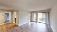 This single-floor residence offers a thoughtfully updated interior with a cohesive design aesthetic carried throughout its living spaces. The open living area is bright and welcoming, featuring light-toned wood-look flooring and neutral gray walls that create a clean, versatile backdrop. A large sliding glass door paired with an adjacent entry door floods the space with natural light and provides direct access to the outdoors, where mature trees are visible through the expansive glazing.

The galley-style kitchen is well-equipped with white shaker cabinetry accented by matte black hardware, white quartz countertops, and a white subway tile backsplash. Stainless steel appliances — including a gas range, refrigerator, and over-the-range microwave — complement the modern aesthetic, while a ceiling fan overhead aids in ventilation and comfort.

The bedrooms feature plush carpeting for added warmth and comfort, with each room receiving natural light through black-framed windows overlooking the wooded surroundings. The primary bedroom includes a spacious reach-in closet. A full bathroom serves the unit, finished with large-format wall tile in the tub/shower surround, accented by a decorative mosaic border strip, and fitted with wood-look flooring and matte black fixtures for a contemporary touch.