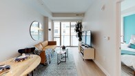 Located at 301 M Street in Washington, DC, this thoughtfully designed unit offers a cohesive modern aesthetic throughout its single floor. The open-concept kitchen is outfitted with two-tone cabinetry — sleek white upper cabinets paired with warm wood-grain lower cabinets — white quartz countertops, a clean tile backsplash, and a full suite of stainless steel appliances including a range, refrigerator, dishwasher, and microwave. Light hardwood-style flooring runs seamlessly throughout, connecting each space with a sense of continuity. The living area is bright and welcoming, anchored by a wall-mounted flat-screen TV and a comfortable seating arrangement, with large sliding glass doors leading to a private balcony that frames views of the surrounding Washington cityscape. The bedroom makes a strong design statement with a bold teal accent wall, large floor-to-ceiling windows that invite natural light and provide city views, and a frosted glass sliding door for added privacy. The bathroom maintains the home's modern character with a floating wood-toned vanity, a framed mirror, full tub-shower combination with white tile surround, and neutral porcelain tile flooring. Throughout the unit, recessed lighting, clean lines, and a carefully curated palette of neutrals and accent tones create a polished, contemporary living environment.