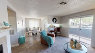 Located at 7000 S Paradise Rd in Las Vegas, Nevada, this single-story home offers a well-connected and functional layout designed for comfortable everyday living. The open-concept main area seamlessly connects the living room, dining space, and kitchen, creating an inviting and cohesive flow throughout. The living room is anchored by a classic brick fireplace, making it a warm focal point for the space. Plush carpeting in the seating areas contrasts with the wood-style hard flooring in the dining and kitchen zones, adding visual interest and definition. The kitchen features a bar-height counter with seating, ideal for casual dining or entertaining, along with a tiled backsplash that adds a clean, finished look. Adjacent to the kitchen, a dedicated dining nook benefits from a pendant light overhead and a window that draws in natural light. Throughout the home, neutral gray walls, textured ceilings, and multiple windows ensure a bright and airy ambiance. Doors on both sides of the space provide convenient access to the outdoors, further enhancing the open and connected feel of this Las Vegas home.
