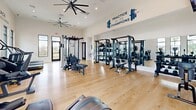 Located at Yardly Drive in Palmetto, Florida, this well-appointed fitness center offers a comprehensive workout facility designed to support a wide range of exercise routines. The space features soaring ceilings equipped with large industrial-style ceiling fans that promote airflow throughout the open floor plan, while recessed lighting ensures consistent illumination across the entire area.

The interior is finished with light hardwood-style flooring that lends warmth and cleanliness to the space. Abundant natural light pours in through large, dark-framed windows lining multiple walls, offering views of the surrounding Florida landscape including palm trees and the community exterior.

The strength training zone is well-stocked with cable machines, multi-functional racks, free weights, kettlebells, medicine balls, and stability balls neatly organized on dedicated storage racks. The cardio section features treadmills, stair climbers, ellipticals, and rowing machines, each positioned to take advantage of the natural light and wall-mounted screens for entertainment.

A dedicated hydration station with a dual-level water fountain is conveniently situated near the entrance. Motivational phrases such as "Practice Makes Champions," "Stronger Than Yesterday," and "Embrace Something New" are displayed prominently on the walls, reinforcing an energizing and encouraging atmosphere throughout the facility.