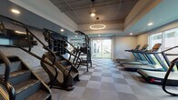 Located on Lankershim Boulevard in North Hollywood, this fitness center offers a comprehensive workout environment spread across a single level, seamlessly blending indoor and outdoor training spaces. The interior is designed with a modern aesthetic, featuring a checkered tile floor, recessed lighting, and a distinctive circular pendant light that anchors the cardio zone. Large floor-to-ceiling windows and sliding glass doors flood the space with natural light while providing direct views of and access to the outdoor turf area.

The cardio section is lined with treadmills, stair climbers, and elliptical machines positioned along the windowed walls, maximizing views and airflow. A dedicated strength training zone houses a multi-station cable machine, barbells, weight plates, and dumbbell racks, complemented by full-length mirrors that enhance the sense of space. A separate room with frosted glass partition walls offers a more private setting for stretching or focused training, fitted with a bench and additional equipment storage.

The outdoor turf area extends the training experience outside, equipped with plyo boxes, medicine balls, kettlebells, and a workout bench — ideal for functional and high-intensity training. The overall ambiance is clean, modern, and purposefully designed to support a wide range of fitness activities.