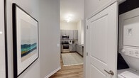 This single-floor residence offers a thoughtfully designed layout with well-defined living spaces and contemporary finishes throughout. The kitchen is outfitted with gray shaker-style cabinetry, granite countertops, a tile backsplash, and a full suite of stainless steel appliances, including a refrigerator, range, and built-in microwave. Wood-look flooring runs through the kitchen and main living areas, lending a cohesive, modern aesthetic.

The living room is bright and inviting, featuring neutral walls, elevated ceilings, and a set of glass doors that open to a private outdoor area, allowing for generous natural light. Two bedrooms are carpeted and each receive natural light through large windows with outdoor views of greenery. Both bedrooms are served by their own walk-in closets equipped with wire shelving systems and hanging rods, providing practical storage solutions.

The full bathroom features a granite-topped vanity with gray cabinetry, a tub-shower combination, and wood-look flooring that complements the rest of the home. A dedicated entry hallway connects the main spaces efficiently, contributing to the overall sense of a well-organized and functional floor plan.