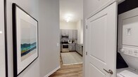 This single-floor residence offers a thoughtfully designed layout with well-defined living spaces and contemporary finishes throughout. The kitchen is outfitted with gray shaker-style cabinetry, granite countertops, a tile backsplash, and a full suite of stainless steel appliances, including a refrigerator, range, and built-in microwave. Wood-look flooring runs through the kitchen and main living areas, lending a cohesive, modern aesthetic.

The living room is bright and inviting, featuring neutral walls, elevated ceilings, and a set of glass doors that open to a private outdoor area, allowing for generous natural light. Two bedrooms are carpeted and each receive natural light through large windows with outdoor views of greenery. Both bedrooms are served by their own walk-in closets equipped with wire shelving systems and hanging rods, providing practical storage solutions.

The full bathroom features a granite-topped vanity with gray cabinetry, a tub-shower combination, and wood-look flooring that complements the rest of the home. A dedicated entry hallway connects the main spaces efficiently, contributing to the overall sense of a well-organized and functional floor plan.
