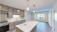 Located at 2536 Rice St in Little Canada, MN, this thoughtfully designed one-bedroom, one-bathroom unit offers a comfortable and modern living experience. The open-concept kitchen is a standout feature, showcasing sleek taupe cabinetry, white quartz countertops, stainless steel appliances including a French door refrigerator, electric range, and dishwasher, as well as a large central island with pendant lighting — ideal for both cooking and casual dining. Light wood-style flooring flows throughout the main living areas, lending a clean, contemporary feel. The bedroom is carpeted for comfort, features a ceiling fan, a large window with outdoor tree views that fill the space with natural light, and includes a walk-in closet with wire shelving for ample storage. The bathroom is finished with light wood-toned cabinetry, a white countertop vanity, and accessibility-friendly grab bars, reflecting a practical and inclusive design. A dedicated in-unit laundry room houses a full-size side-by-side washer and dryer set along with additional wire shelving for storage. The unit's neutral color palette and modern finishes create a bright, welcoming ambiance throughout.