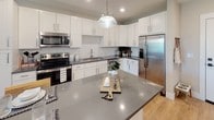 Located at 9235 Senator Royall Dr. in Charlotte, NC, this single-floor residence offers a thoughtfully designed layout with modern finishes throughout. The kitchen is a standout feature, showcasing white shaker cabinetry, subway tile backsplash, stainless steel appliances, and a large island with a sleek gray quartz countertop — ideal for both cooking and casual dining. Pendant lighting and recessed fixtures illuminate the space, which flows seamlessly over warm wood-look flooring.

The living area exudes a welcoming ambiance with soft, neutral wall tones, a decorative area rug, and generous natural light filtering through window treatments. Thoughtful décor accents, including framed wall art, complete the space.

The primary bedroom is a restful retreat, featuring plush carpet, a ceiling fan, and large windows that invite natural light and views of the surrounding greenery. An adjacent en-suite bathroom provides a double-sink vanity with gray countertops, white cabinetry, wood-look flooring, and a glass-enclosed shower alongside a soaking tub. An additional bedroom offers the same calm aesthetic, with direct access to a well-appointed bathroom. This residence combines functional design with contemporary style throughout.