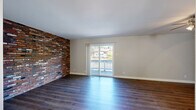 This multi-level home spans three floors and offers a well-organized layout with two bedrooms, three bathrooms, a living room, family room, kitchen, pantry, and a patio. The main living areas are defined by striking full-height exposed brick accent walls that serve as a bold architectural centerpiece throughout multiple rooms. Rich hardwood-style flooring flows through the living and family rooms, complemented by sliding glass doors that open to a private patio with outdoor views, filling the space with natural light.

The kitchen is well-appointed with dark cabinetry, granite-look countertops, a tile backsplash, and wood-style flooring, while an adjacent pantry provides additional storage. The bathrooms echo the kitchen's design language, featuring dark vanities with light countertops and clean tile finishes.

The primary bedroom is generously sized with plush carpeting, a ceiling fan, an accent brick wall, and access to a private en-suite bathroom and a walk-in closet with built-in wire shelving. Carpeted staircases with warm wood railings connect all three floors, with open-tread detailing that adds visual interest. Additional closets and a utility room contribute to the home's practical storage capacity throughout.