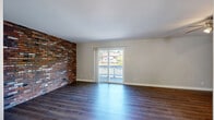 This multi-level home spans three floors and offers a well-organized layout with two bedrooms, three bathrooms, a living room, family room, kitchen, pantry, and a patio. The main living areas are defined by striking full-height exposed brick accent walls that serve as a bold architectural centerpiece throughout multiple rooms. Rich hardwood-style flooring flows through the living and family rooms, complemented by sliding glass doors that open to a private patio with outdoor views, filling the space with natural light.

The kitchen is well-appointed with dark cabinetry, granite-look countertops, a tile backsplash, and wood-style flooring, while an adjacent pantry provides additional storage. The bathrooms echo the kitchen's design language, featuring dark vanities with light countertops and clean tile finishes.

The primary bedroom is generously sized with plush carpeting, a ceiling fan, an accent brick wall, and access to a private en-suite bathroom and a walk-in closet with built-in wire shelving. Carpeted staircases with warm wood railings connect all three floors, with open-tread detailing that adds visual interest. Additional closets and a utility room contribute to the home's practical storage capacity throughout.
