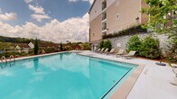 Located in the Ardmore Park neighborhood of Atlanta, Georgia, this outdoor amenity space centers around a generously sized swimming pool with crystal-clear blue water. The pool deck is lined with modern chaise lounge chairs, providing ample space for sunbathing and relaxation. A striking large-scale beach mural adorns the adjacent wall, creating a resort-like atmosphere that adds a vivid artistic element to the outdoor setting.

The surrounding landscape is thoughtfully designed, featuring a variety of mature trees, flowering shrubs, hydrangeas, and evergreen plantings set against mulched garden beds. Iron fencing borders the perimeter of the space, offering both security and open views of the surrounding tree canopy and neighboring community. Bollard lighting is integrated throughout the landscaping, ensuring the area is well-lit for evening use.

Seating areas with chairs and tables are tucked into garden nooks, offering quieter spots for outdoor enjoyment. The lush greenery and carefully maintained plantings contribute to a park-like ambiance. Open skies and views of the wooded surroundings enhance the sense of escape within this well-appointed community outdoor space in the heart of Atlanta.