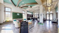 Located at 250 Cherry Ridge Dr in Jacksonville, FL, this single-floor community clubhouse at Oakleaf Plantation offers a well-appointed and inviting gathering space. The open-concept layout seamlessly connects the living, dining, and kitchen areas, all unified by rich hardwood-style flooring and a striking teal and white color palette that lends a fresh, modern aesthetic throughout.

Soaring ceilings with elegantly curved architectural beam details define the central living lounge, which is bathed in natural light from expansive floor-to-ceiling windows offering views of the surrounding landscape. A striking living green wall, illuminated with the Oakleaf Plantation logo, serves as a bold focal point, complemented by stylish pendant lighting and an inviting arrangement of seating.

The fully equipped kitchen features dark espresso cabinetry, a mosaic tile backsplash, light stone countertops, stainless steel appliances, and a curved island with bar seating. Adjacent to the kitchen, the dining area provides a mix of formal table seating and high-top bistro tables, with large glass doors opening directly to the outdoors.

A dedicated office area offers multiple individual workstations with computers, pendant lighting, and a quiet, focused environment. Throughout the space, abundant natural light, high ceilings, and thoughtfully curated furnishings combine to create a welcoming and functional community hub.