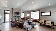 Located at 3156 North Guinness Lane in Post Falls, Idaho, this single-story clubhouse offers a thoughtfully designed gathering space with a range of functional amenities. The main lounge area is defined by soaring vaulted ceilings with recessed lighting and a dramatic floor-to-ceiling stacked stone fireplace, which anchors the room and serves as a striking focal point. Light hardwood flooring flows throughout, complementing the neutral gray walls and dark-trimmed windows that frame abundant natural light from multiple large windows.

The lounge accommodates varied seating arrangements, including rich brown leather sofas and armchairs alongside bold patterned accent chairs with matching ottomans. A dedicated dining area features a formal table with upholstered seating, while a separate intimate dining nook with a round table and red chairs is tucked alongside the stone wall.

The full kitchen is equipped with dark espresso cabinetry, granite countertops, stainless steel appliances including a range, microwave, dishwasher, and refrigerator, and a wall-mounted range hood. A fitness room with exercise equipment is accessible through a glass-paneled door near a wall-mounted water fountain. An ADA-accessible restroom with stone tile surround and grab bars completes the facility's practical offerings.