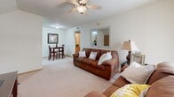 This apartment at The Flats in Searcy, Arkansas, offers a well-organized single-floor layout designed for comfortable everyday living. The living room serves as the central gathering space, featuring plush wall-to-wall carpeting, a ceiling fan with light fixture, and a large window with vertical blinds that allows natural light to fill the room. The space flows naturally into a dedicated dining area, which accommodates a full dining table and chairs beneath warm, neutral-toned walls. The galley-style kitchen is efficiently designed with oak cabinetry, granite-look countertops, tile flooring, and a full suite of white appliances including a range, refrigerator, microwave, and dishwasher. A stainless steel sink and an arched window accent add character to the space. The unit includes two carpeted bedrooms, each offering closet storage. One bedroom features a window with outdoor views and warm natural light, while the other provides a cozy, private retreat. The full bathroom is finished with tile flooring, a granite-topped vanity with oak cabinetry, and a shower-tub combination. In-unit laundry connections are also available, adding everyday convenience to this functional and inviting apartment home.