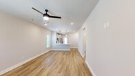 This single-story home in Madison, Alabama offers a clean, modern aesthetic with a thoughtfully designed open-concept floor plan. The combined living room and kitchen area serves as the heart of the home, featuring warm wood-look luxury vinyl plank flooring that runs consistently throughout the entire space. The living area is fitted with a ceiling fan and recessed lighting, while natural light filters in through a window with blinds. The kitchen includes white cabinetry with dark hardware, a stainless steel refrigerator, pendant lighting over a central island or bar, and a full-light exterior door that adds additional brightness and backyard access. The three bedrooms are well-proportioned, each featuring ceiling fans, recessed lighting, neutral warm-toned walls, and window treatments. The primary bedroom includes a dedicated walk-in closet with wire shelving and hanging rods. Secondary bedrooms are served by a standard closet with built-in hanging storage. The two bathrooms are finished in a contemporary style; one features a walk-in glass shower, white vanity with a solid-surface countertop, dark oil-rubbed bronze fixtures, and a framed mirror. A hallway connects the bedroom wing to the main living areas, completing the functional and cohesive layout of this move-in ready home.