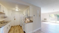 Located at 1 Apple Rd in Beverly, Massachusetts, this single-floor unit offers a clean, modern living experience with thoughtful design throughout. The open-concept living area is bathed in natural light from large sliding glass doors that lead to a private balcony with greenery views. Light wood-style flooring flows throughout the main living spaces, complemented by crisp white trim and neutral-toned walls, including a bold charcoal accent wall that anchors the living room.

The galley-style kitchen is well-equipped with white cabinetry, granite-style countertops, and white appliances including a range, microwave, and refrigerator. A deep sink and ample upper and lower cabinet storage make this an efficient and functional cooking space, finished with the same light wood-style flooring as the rest of the unit.

The bedroom area is generously sized and features a large walk-in closet outfitted with dual hanging rods and shelving on both sides, providing exceptional storage capacity. Carpet flooring adds comfort underfoot within the closet.

The bathroom offers a clean, updated aesthetic with a white vanity, undermount sink, chrome hardware, and a large mirror. Light wood flooring continues here, maintaining a cohesive look. A textured ceiling in the kitchen area and flush-mount lighting throughout complete this move-in ready space.