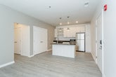 This thoughtfully designed single-floor residence combines modern aesthetics with functional living. The kitchen serves as the heart of the space, showcasing white shaker-style cabinetry with open shelving, dark countertops, and a full suite of stainless steel appliances including a refrigerator, range with oven, and built-in microwave. A central island with a dark countertop and integrated sink provides additional prep space and is illuminated by stylish pendant lighting above. Light wood-style flooring extends throughout the main living areas, lending a clean, contemporary feel. An in-unit washer is also conveniently accessible from the kitchen area. The bedrooms feature neutral-toned carpet and bright white walls, offering a calm and versatile environment. Closet storage is included in at least one bedroom. The bathrooms reflect a consistent modern palette — one features a white vanity with ample cabinetry and light wood-style flooring, while another is designed with accessibility in mind, equipped with grab bars and an open shower area. Throughout the residence, recessed lighting and clean white walls create a bright, welcoming ambiance that complements the unit's crisp, contemporary design.