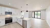 This contemporary single-floor residence offers 3 bedrooms and 2 bathrooms thoughtfully arranged for comfortable living. The open-concept kitchen and living area serves as the heart of the home, featuring white shaker cabinetry with black hardware, a classic subway tile backsplash, a central island with a stainless steel sink, and a full suite of stainless steel appliances including a refrigerator, range, microwave, and dishwasher. Stylish black dome pendant lights hang above the island, complementing the modern aesthetic. Light luxury vinyl plank flooring flows throughout the entire residence, creating a cohesive and easy-to-maintain surface. The living area is bright and open, with recessed lighting and large black-framed sliding glass doors that lead to a private balcony with outdoor views. The bedrooms are well-proportioned, each offering large black-framed windows that fill the rooms with natural light. The spacious primary bedroom includes a dedicated walk-in closet outfitted with dual hanging rods and built-in shelving. Both bathrooms are finished in a clean white palette, with one featuring penny mosaic tile flooring, a soaking tub, and black fixtures. A dedicated laundry room with a full-size washer and dryer and overhead shelving adds everyday convenience.