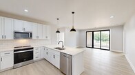 This contemporary single-floor residence offers 3 bedrooms and 2 bathrooms thoughtfully arranged for comfortable living. The open-concept kitchen and living area serves as the heart of the home, featuring white shaker cabinetry with black hardware, a classic subway tile backsplash, a central island with a stainless steel sink, and a full suite of stainless steel appliances including a refrigerator, range, microwave, and dishwasher. Stylish black dome pendant lights hang above the island, complementing the modern aesthetic. Light luxury vinyl plank flooring flows throughout the entire residence, creating a cohesive and easy-to-maintain surface. The living area is bright and open, with recessed lighting and large black-framed sliding glass doors that lead to a private balcony with outdoor views. The bedrooms are well-proportioned, each offering large black-framed windows that fill the rooms with natural light. The spacious primary bedroom includes a dedicated walk-in closet outfitted with dual hanging rods and built-in shelving. Both bathrooms are finished in a clean white palette, with one featuring penny mosaic tile flooring, a soaking tub, and black fixtures. A dedicated laundry room with a full-size washer and dryer and overhead shelving adds everyday convenience.