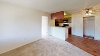 This single-floor residential unit offers a functional and well-organized layout across several distinct living areas. The open-concept living and dining space features neutral wall tones, plush wall-to-wall carpeting, and a textured ceiling. A front entry door with sidelight allows natural light to filter into the main living area, which flows seamlessly toward the kitchen.

The kitchen is equipped with warm medium-toned wood cabinetry, black appliances including a full-size refrigerator, range, and over-the-range microwave, as well as a sink and light-toned countertops. A peninsula with bar-height overhang separates the kitchen from the living area, offering additional prep space and casual seating potential. Durable wood-look flooring runs throughout the kitchen, adding a contrasting warmth to the carpeted living spaces.

The bedrooms are generously proportioned, carpeted, and receive natural light through windows that overlook the surrounding exterior. One bedroom includes an en-suite bathroom access and a dedicated closet. Both bathrooms feature full tub-shower combinations with clean white surrounds and chrome fixtures, maintaining a consistent and practical aesthetic throughout.

Overall, the unit presents a clean, neutral palette with a straightforward layout well-suited for comfortable everyday living.