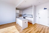 Located at 69-02 Queens Blvd in Woodside, NY, this thoughtfully designed one-bedroom, one-bathroom unit offers a modern living experience across a single floor. The open-concept layout makes efficient use of the space, with warm-toned hardwood flooring flowing seamlessly throughout.

The kitchen is a standout feature, showcasing flat-front white cabinetry that extends to the ceiling, stainless steel appliances including a full-size range and refrigerator, a black matte faucet, and a central island with a clean quartz countertop — ideal for both cooking and casual dining. Recessed lighting overhead keeps the space bright and contemporary.

The bedroom is a comfortable, sun-filled retreat with large windows that allow generous natural light to pour in. A dedicated closet with built-in shelving and hanging rods provides practical storage. The room's clean white walls and hardwood floors maintain the unit's cohesive modern aesthetic.

The bathroom is elegantly appointed with large-format beige floor tiles, floor-to-ceiling marble-style wall tiles surrounding the soaking tub and shower combination, a floating wood-toned vanity with a white undermount sink, and black matte fixtures throughout — lending a refined, spa-like atmosphere.

A dedicated closet space adds further storage convenience. The unit's clean lines, neutral palette, and quality finishes throughout make it a polished and move-in-ready Woodside residence.