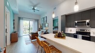 Located at 600 N Pine Island Rd in Plantation, FL, this single-floor residence offers a thoughtfully designed open-concept layout that seamlessly connects the kitchen, dining, and living areas. The kitchen is a standout feature, equipped with sleek gray shaker-style cabinetry, white quartz countertops, stainless steel appliances including a full-size refrigerator, range, microwave, and dishwasher, a white subway tile backsplash, and a large central island with pendant lighting perfect for casual dining. Light wood-look flooring runs throughout the main living areas, enhancing the bright and airy atmosphere. The living room is generously proportioned with a ceiling fan overhead and sliding glass doors that open to a private balcony with greenery views. The primary bedroom features soft carpeting and calming teal-toned walls, with natural light filtering through large windows. A second bedroom provides versatile space, also highlighted by a bold teal accent wall. Both bathrooms are finished with large-format tile flooring, gray vanity cabinetry, white quartz countertops, and walk-in closet access. The overall ambiance is contemporary and inviting, with a cohesive coastal-inspired palette throughout.
