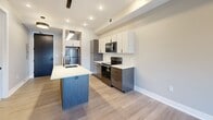 This well-designed one-bedroom, one-bathroom unit offers a thoughtful and efficient layout across a single floor. The open-concept kitchen serves as the heart of the space, showcasing two-tone cabinetry with white upper cabinets and warm wood-toned lower cabinets, a subway tile backsplash, and a full suite of stainless steel appliances including a refrigerator, electric range, and over-the-range microwave. A central kitchen island with a light quartz countertop and an undermount sink with a sleek gooseneck faucet provides additional workspace and casual dining potential. Light wood-style flooring runs throughout the main living areas, contributing to a clean and contemporary aesthetic. Recessed lighting and a modern pendant fixture illuminate the kitchen and living area, which opens to a private balcony through large sliding glass doors, inviting natural light and outdoor views. The bedroom features plush carpet flooring, a ceiling fan, a large window with exterior views, and recessed lighting, creating a comfortable retreat. The bathroom is finished with neutral tile flooring and walls, and includes a glass-enclosed walk-in shower with matte black fixtures, offering a clean, modern feel. A dedicated closet and hallway complete this efficiently designed unit.