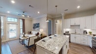 This well-appointed two-bedroom, two-bathroom residence in Houston, TX offers a thoughtfully designed single-floor layout that blends modern finishes with a warm, neutral aesthetic. The open-concept living and kitchen area serves as the heart of the home, where wood-look flooring, crown molding, and recessed lighting create an inviting atmosphere. The kitchen is a standout feature, showcasing white shaker cabinetry, a classic subway tile backsplash, stainless steel appliances, and a large granite-topped island with seating — ideal for casual dining or entertaining. Pendant lighting above the island adds a refined touch. The living room offers natural light through large windows with views of the surrounding area, complemented by a ceiling fan and ample space for comfortable furnishings. Both bedrooms are generously sized, each with large windows that invite natural light. The primary suite connects to a spa-inspired bathroom featuring marble-look tile flooring, a granite double vanity with gold-toned fixtures, a spacious glass-enclosed shower, and a walk-in closet. The second bathroom mirrors the same elevated design with a granite vanity, marble-style tile, and a soaking tub with shower combo.
