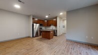 This single-floor residence offers a thoughtfully designed layout that balances open living areas with comfortable private spaces. The kitchen serves as a central highlight, featuring rich warm-toned cabinetry, granite countertops, a center island, and a full suite of stainless steel appliances including a refrigerator, range, microwave, and dishwasher. Recessed lighting illuminates the space, which flows seamlessly into an open living area finished with durable hardwood-style flooring throughout. The living area benefits from a sliding glass door that opens to an outdoor patio, inviting natural light and providing views of surrounding greenery. The bedrooms are finished with soft, neutral carpeting and feature generous closet space, including a double-door closet in one room, along with windows that bring in additional natural light. Two bathrooms serve the unit: a full bathroom featuring large-format stone-look tile, a combination tub and shower with elegant tile surround, and warm wood cabinetry; and a second bathroom with a glass-enclosed shower, vanity with under-sink storage, and a window for natural ventilation. Neutral wall tones throughout create a clean, cohesive aesthetic that complements the warm wood finishes and tile accents present across the space.