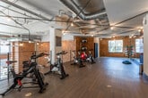 Located at 951 Glenwood Ave SE in Atlanta's vibrant Glenwood Park neighborhood, this fitness facility combines industrial-chic design with a fully equipped workout environment. Exposed brick walls, visible ductwork, and Edison bulb track lighting lend the space a distinctive loft-like character, while wide-plank hardwood flooring runs throughout, adding warmth and durability underfoot.

The main exercise floor is generously proportioned, featuring floor-to-ceiling mirrors along one wall that amplify natural light streaming in through large windows. The mirrored studio area is well-suited for group fitness classes, yoga, or functional training, and is equipped with BOSU balance trainers and a rack of weighted medicine balls. A curated art piece adorns one accent wall, adding a creative focal point to the workout environment.

An open cycling area houses multiple stationary spin bikes, complemented by stability balls and additional fitness accessories neatly organized along the exposed brick walls. An upper mezzanine level, accessible via a staircase with sleek black metal railings, provides an elevated vantage point overlooking the main floor and features additional equipment. The interplay of natural light, reflective mirrors, and industrial architectural elements creates a motivating, energetic atmosphere throughout the facility.