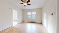 Located at 1006 W 22nd St in Minneapolis, Minnesota, this 2-bedroom, 1-bathroom unit offers a practical and efficient single-floor layout. Light hardwood flooring runs consistently throughout the living areas and bedrooms, creating a bright, cohesive feel. The spacious primary bedroom is notably generous for the overall footprint, featuring a ceiling fan with light fixture, double windows that allow ample natural light, and baseboard heating for year-round comfort. The second bedroom also benefits from multiple windows with outdoor views of the surrounding neighborhood and baseboard heating. The living area is open and airy, with a ceiling fan, side window, and direct sightlines to both the kitchen and entryway. The kitchen is compact and functional, equipped with a gas range, refrigerator, wood-toned cabinetry, and a light countertop with sink. The bathroom features clean, neutral finishes with a wall-mounted sink, toilet, a framed vanity mirror, and tiled flooring. Baseboard heating is present throughout the unit, ensuring consistent warmth. The overall aesthetic is clean and minimal, with cream-toned walls and white trim providing a neutral canvas throughout the space.