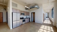 Located at 443 San Pedro St in the heart of downtown Los Angeles, this single-floor loft-style space blends industrial character with modern finishes throughout. The open layout is anchored by polished concrete floors and soaring ceilings that lend a sense of expansive volume. Exposed spiral ductwork and structural beams overhead underscore the raw, urban aesthetic that defines the space.

The kitchen is thoughtfully designed with wood-toned cabinetry, dark countertops, and a full suite of stainless steel appliances including a refrigerator, range, microwave, and dishwasher. A white tile backsplash adds a clean contrast to the warm cabinetry tones. The kitchen flows seamlessly into the open living area, making the space well-suited for both everyday use and entertaining.

A generously sized main room features large, multi-pane black-framed windows set against white-painted brick walls, flooding the interior with abundant natural light and offering an airy, gallery-like atmosphere. An additional private room provides a quiet, versatile space with its own HVAC vent and clean white walls.

The bathrooms are finished with modern fixtures, including a wood-vanity with dark countertop, wall-mounted mirror, and sleek black hardware. The overall ambiance is contemporary urban, combining utilitarian design elements with clean, modern touches throughout.